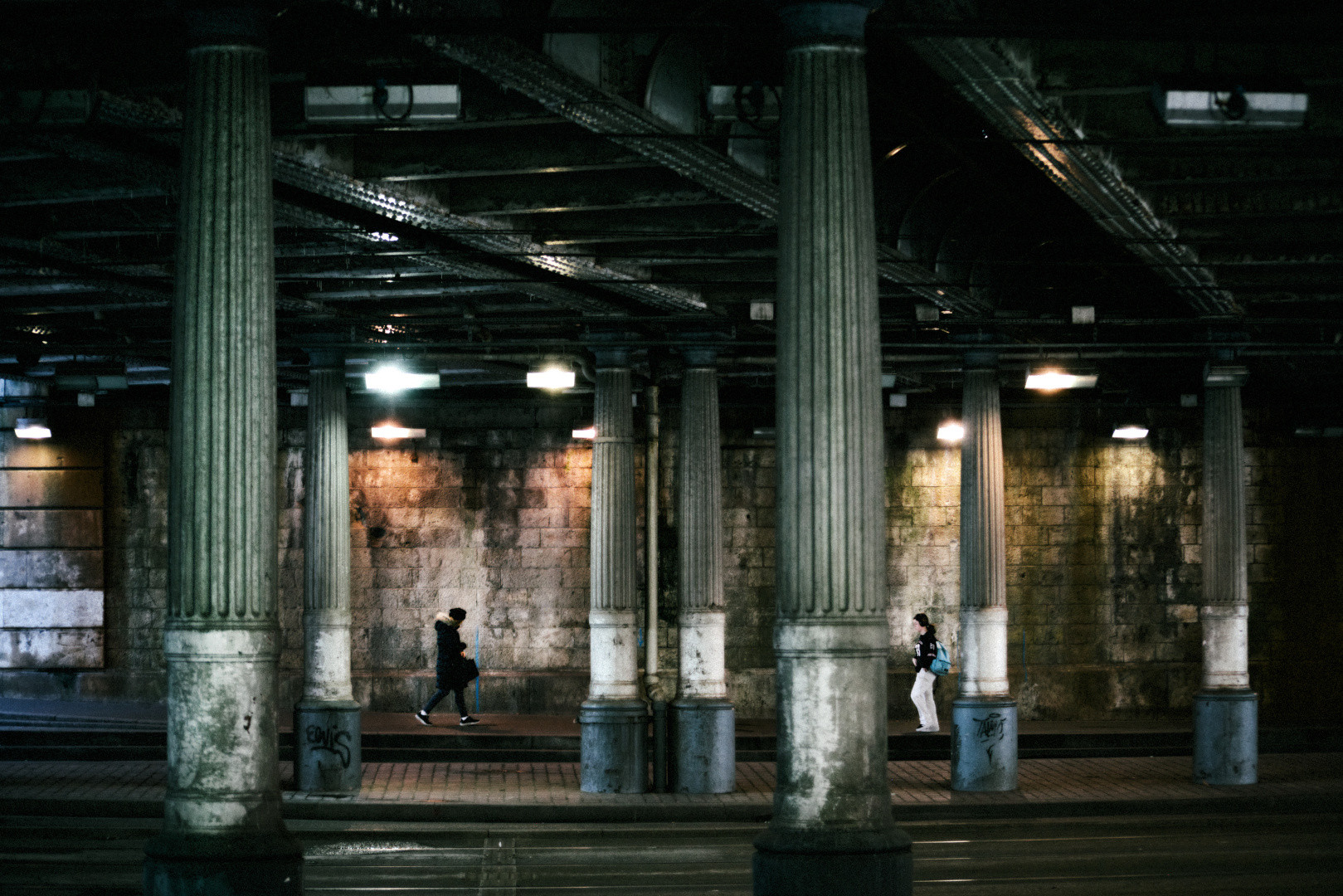 An underpass with towering columns, artificial light, and deep shadows