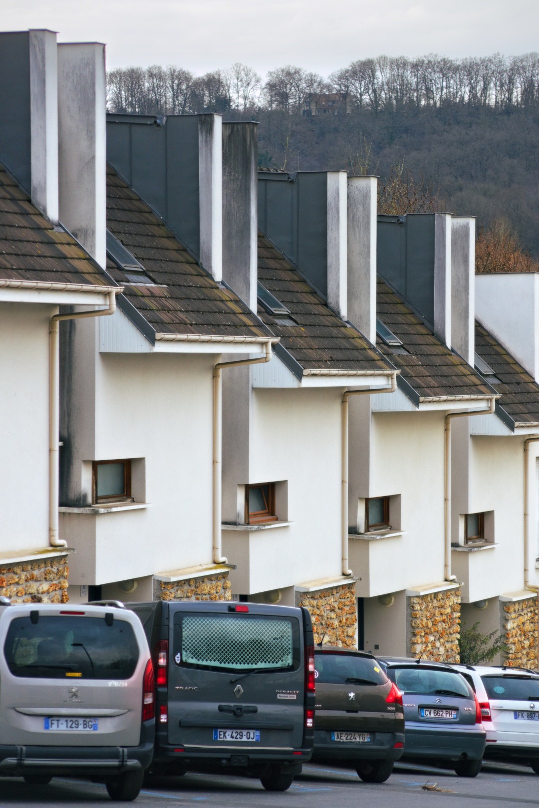 A repeating row of white houses and chimneys above parked cars